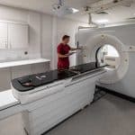 PET-CT scanner in a clinical room with a healthcare professional preparing the machine for a diagnostic imaging procedure.