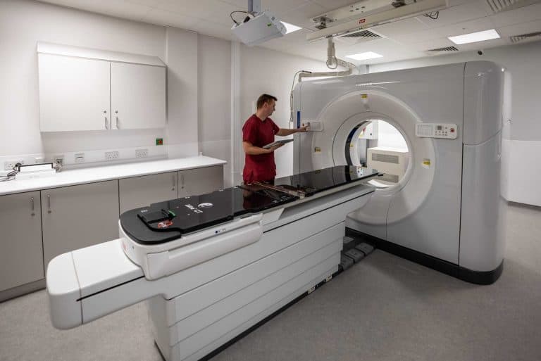 PET-CT scanner in a clinical room with a healthcare professional preparing the machine for a diagnostic imaging procedure.