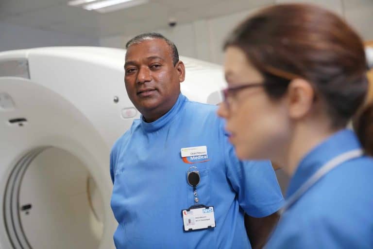 Healthcare professionals in blue uniforms standing beside a PET-CT scanner during a clinical training session, demonstrating teamwork and team resilience in medical imaging.
