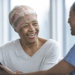 Healthcare professional speaking with a patient while holding a digital tablet in a bright clinical setting.