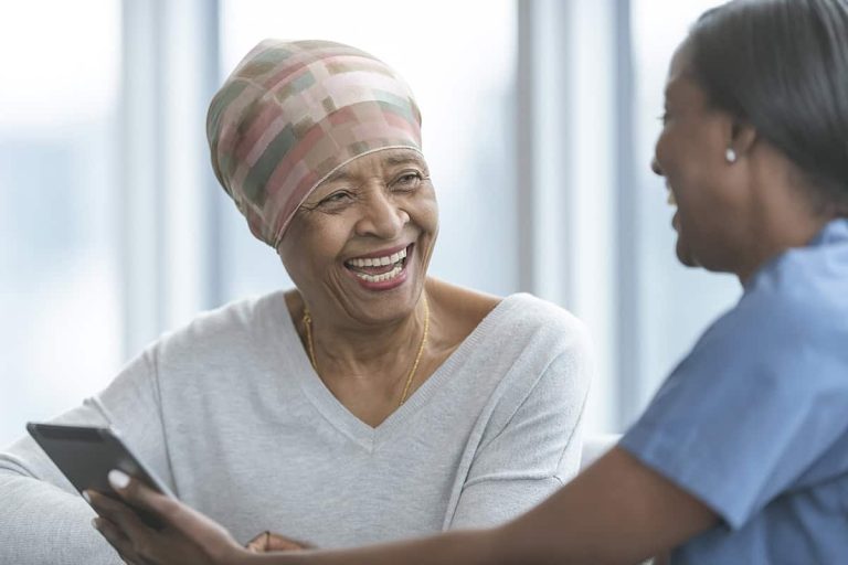 Healthcare professional speaking with a patient while holding a digital tablet in a bright clinical setting.