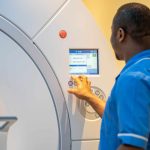 Medical professional operating a PET-CT scanner, adjusting settings on the machine’s control panel in a clinical environment.