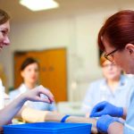 Healthcare professionals practicing IV cannulation technique on a patient’s arm during a hands-on clinical training session.