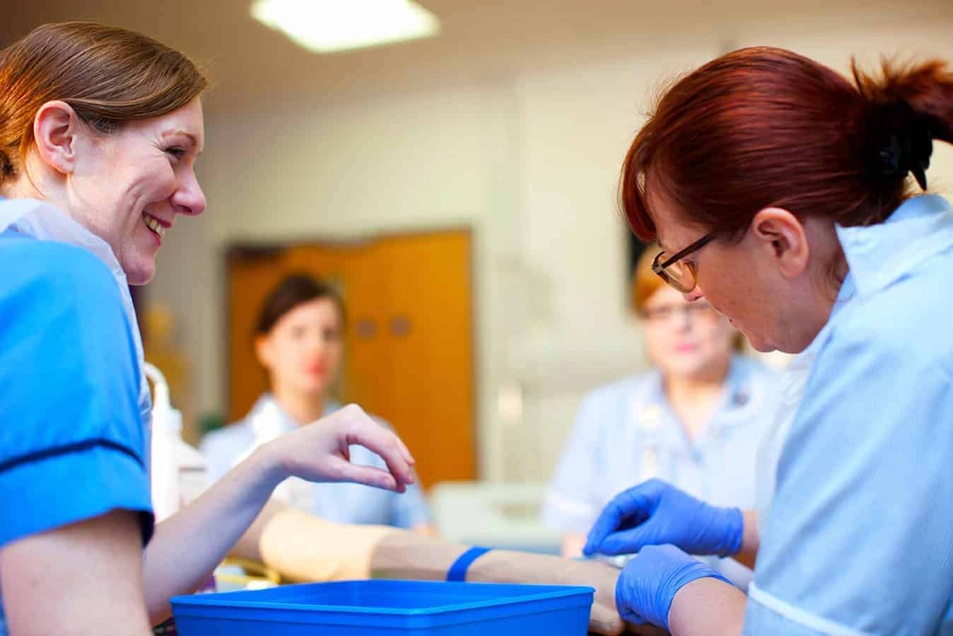 Healthcare professionals practicing IV cannulation technique on a patient’s arm during a hands-on clinical training session.