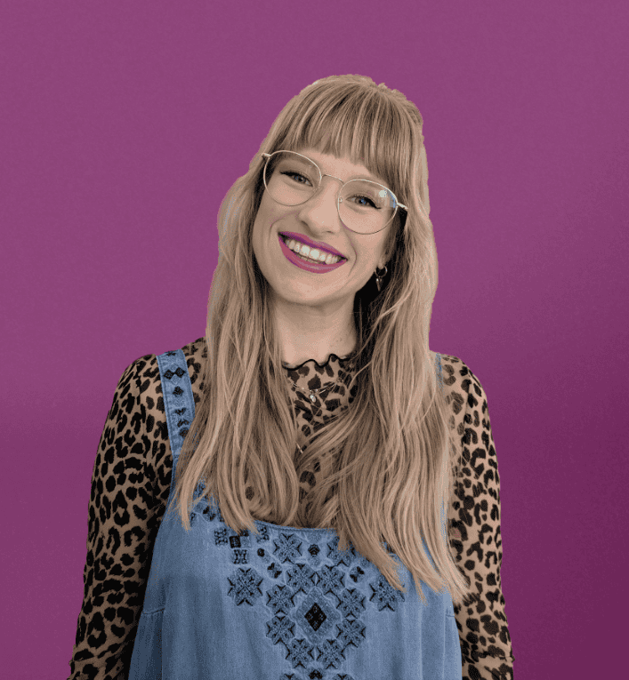 Expert woman with long blonde hair, wearing glasses, a leopard print top, and a denim dress, smiling against a solid purple background.