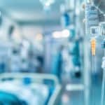 Vial with medication or solution being prepared in a clinical setting, healthcare professional handling medical supplies, medical equipment, hospital or laboratory environment.