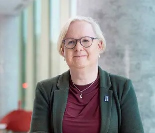 Modern woman with glasses, wearing a blazer and personal badge, in a professional setting at The Christie PET-CT Academy, highlighting leadership and expertise in medical imaging and PET-CT training.